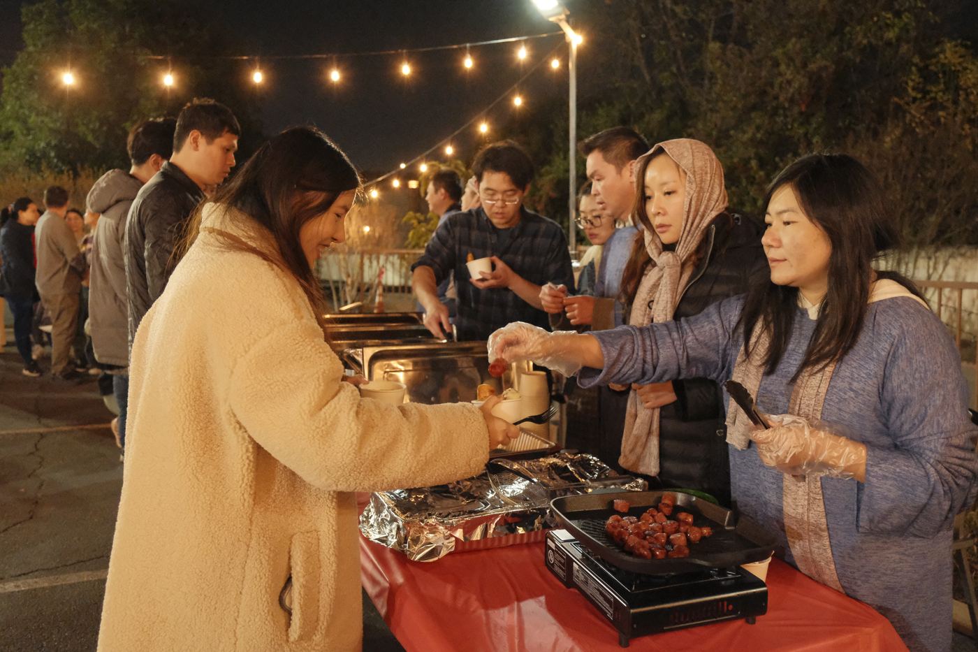 People lining up for food under string lights