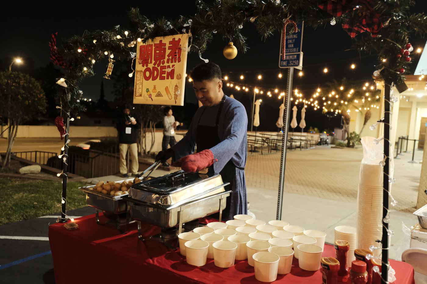 Food stalls under string lights, with a volunteer preparing hot food